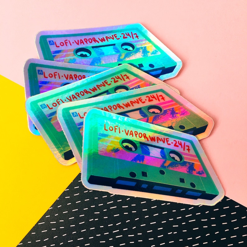 May include: A stack of five iridescent holographic stickers featuring a cassette tape with the text "LOFI-VAPORWAVE-24/7" in red. The stickers are on a pink and yellow background.