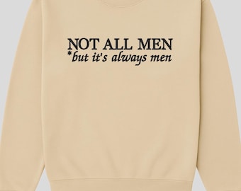 以下が含まれることがあります： 「NOT ALL MEN *but it's always men」の黒い文字がプリントされたベージュのスウェットシャツ。クルーネックと長袖です。ブランド名は背面上部にピンク色で表示されています。
