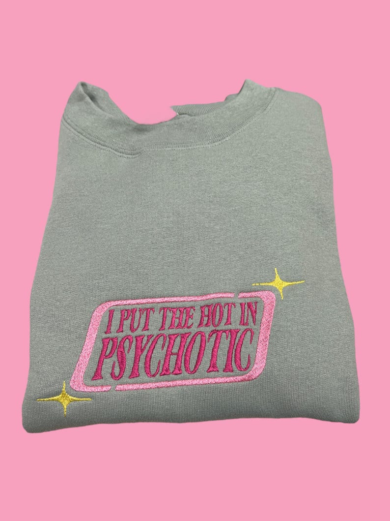 A gray sweatshirt with a pink and yellow embroidered phrase that reads "I PUT THE HOT IN PSYCHOTIC" on it.
