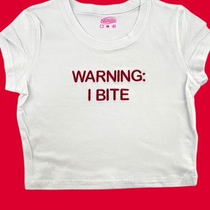 May include: White cropped t-shirt with red embroidered text that reads "WARNING: I BITE"
