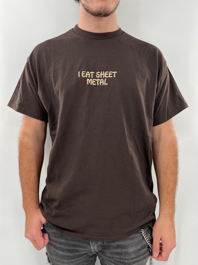 Op de afbeelding: Een bruin T-shirt met de tekst "I EAT SHEET METAL" in lichtbruine kleur op de voorkant.