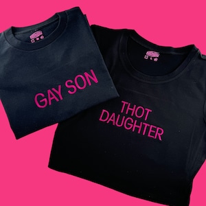 May include: Two black t-shirts with pink lettering. The top shirt says "Gay Son" and the bottom shirt says "Thot Daughter".
