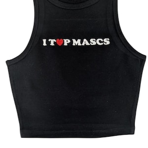 May include: Black crop top with the text "I ❤️ TOP MASCS" in white letters and a red heart. The top has a scoop neck and is sleeveless. A small logo is visible at the top.