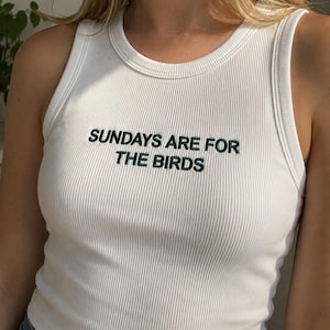 A woman wearing a white tank top with the text "SUNDAYS ARE FOR THE BIRDS" printed on it.