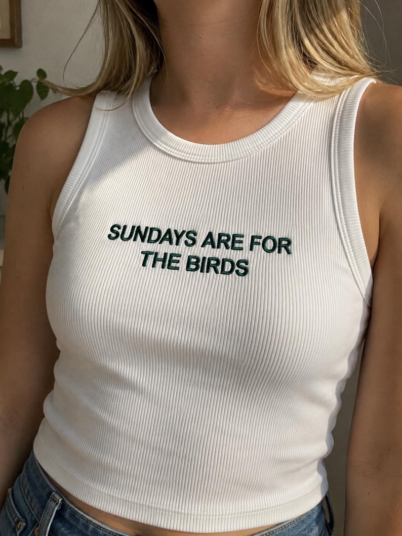 A woman wearing a white tank top with the text "SUNDAYS ARE FOR THE BIRDS" printed on it.