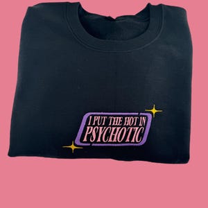 A black sweatshirt with a purple and yellow graphic on the front, which says "I PUT THE HOT IN PSYCHOTIC" in a stylized font.
