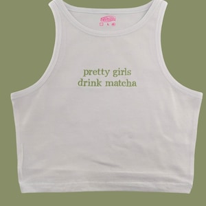 May include: A white cropped tank top with the text "pretty girls drink matcha" in green embroidery.