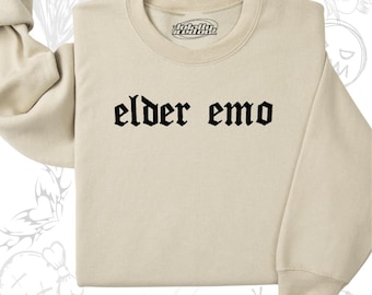 Puede incluir: Una sudadera beige con el texto "elder emo" impreso en fuente gótica negra.