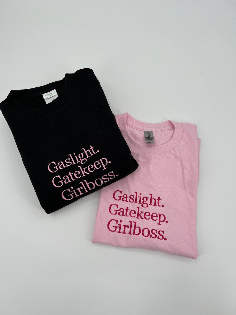 Puede incluir: Dos camisetas con el texto "Gaslight. Gatekeep. Girlboss." impreso en ellas. Una camiseta es negra con texto rosa y la otra es rosa con texto rosa oscuro.