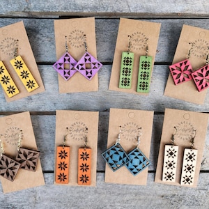 May include: A collection of wooden earrings in various colors, including yellow, purple, green, pink, brown, orange, blue, and natural wood. Each pair features unique geometric and floral designs. The earrings are displayed on brown cards.