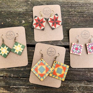 May include: Four pairs of handmade wooden earrings with different quilt block patterns. The earrings are displayed on brown card stock with the text "The Crafty Journey" printed on each card.