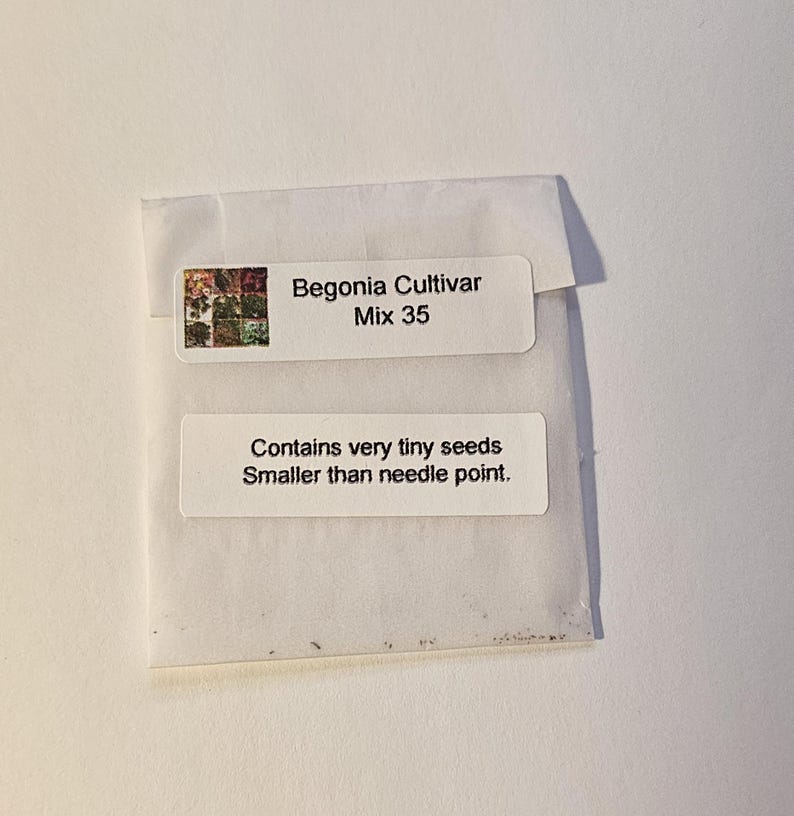May include: A small white seed packet with the text "Begonia Cultivar Mix 35" and "Contains very tiny seeds Smaller than needle point." The packet has a small image of colorful flowers.