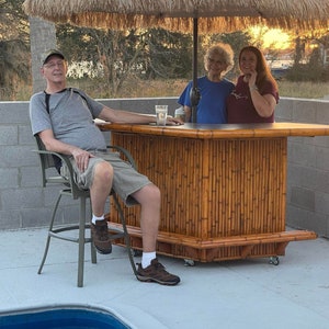 Bamboo tiki bar. Thatch umbrella and fitted outdoor cover included. Backyard patio deck bar with storage, wheels, footrail and electrical.