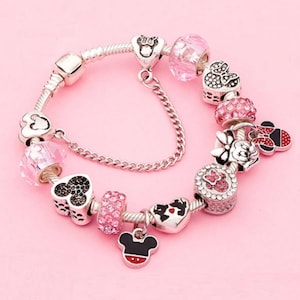 Puede incluir: Un brazalete de plata con dijes de color rosa y rojo con los personajes de Mickey Mouse y Minnie Mouse. El brazalete tiene una cadena de plata y un cierre de seguridad.