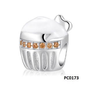 May include: Silver charm in the shape of a cupcake with white icing and brown crystal accents. The charm has a small heart on top and a textured base. PC0173