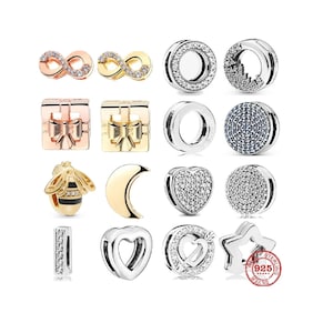 Könnte beinhalten: Eine Sammlung von 14 silbernen, goldenen und roségoldenen Charm-Perlen mit verschiedenen Designs, darunter Unendlichkeitszeichen, Schleifen, Herzen, Sterne, Monde und Bienen. Die Perlen sind mit klaren und blauen Zirkonia-Steinen verziert.