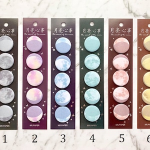 May include: Six sets of decorative paper stickers, each with a moon phase design. The colour schemes vary, including grey, purple, blue, green, pink, and yellow. The text "The secret of the moon" and Chinese characters are printed on the top of each sheet.