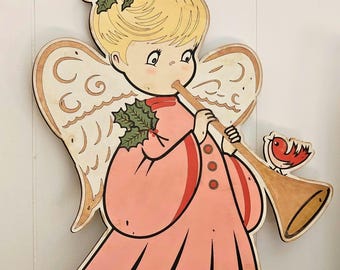 May include: Wooden angel Christmas decoration. The angel is wearing a pink dress and playing a trumpet. The angel has blonde hair and wings. A red bird is perched on the trumpet. The angel is decorated with holly and a red bow.