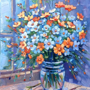 May include: A bouquet of blue and orange wildflowers in a clear glass vase on a wooden table. The flowers are arranged in a loose, natural style, and the vase is simple and elegant.