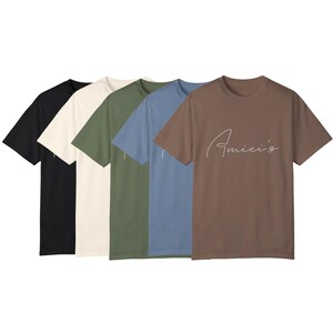 May include: A collection of five short-sleeved t-shirts in various colors: black, off-white, olive green, blue, and brown. The brown shirt features the cursive text "Amici's" in white. The shirts are made of a soft, comfortable material.