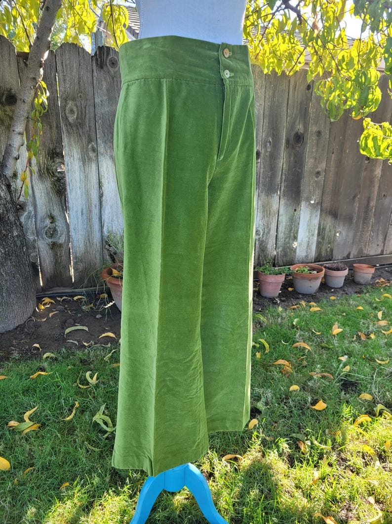 Puede incluir: Pantalones verdes brillantes, de cintura alta y pernera ancha. Los pantalones tienen cierre de bot&oacute;n y parte delantera plisada. La tela tiene una textura suave y aterciopelada. Los pantalones se exhiben en un maniqu&iacute; azul en exteriores.