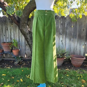 Puede incluir: Pantalones de pana verde lima con cintura alta y perneras anchas. Los pantalones se exhiben en un maniqu&iacute; con una parte superior blanca, sobre un fondo de valla de madera y vegetaci&oacute;n.
