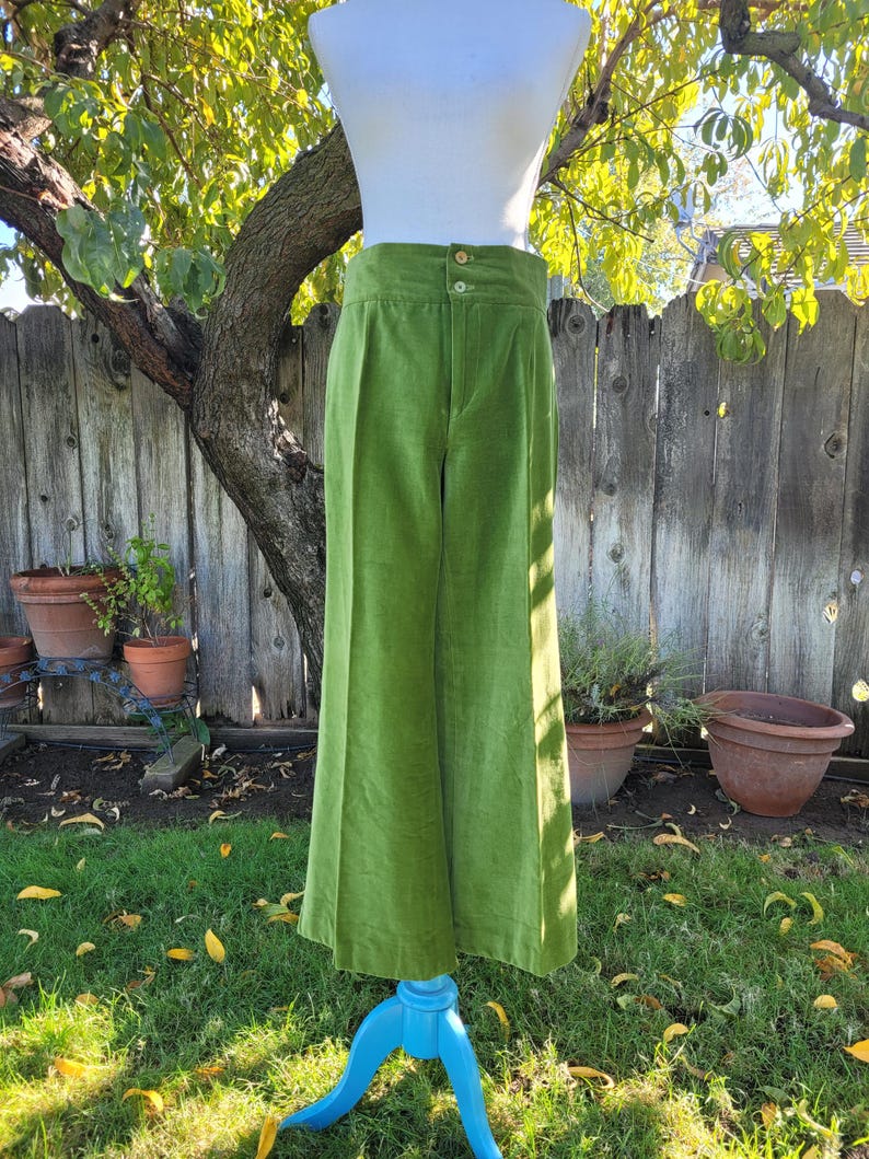 Puede incluir: Pantalones de pana verde lima con cintura alta y perneras anchas. Los pantalones se exhiben en un maniqu&iacute; con una parte superior blanca, sobre un fondo de valla de madera y vegetaci&oacute;n.