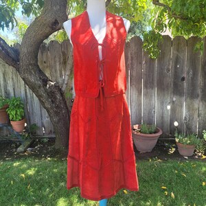 May include: A bright red two-piece set consisting of a sleeveless vest and a matching skirt. The vest features a V-neckline with three tie closures down the front. The skirt has a paneled design with visible stitching details throughout the fabric.