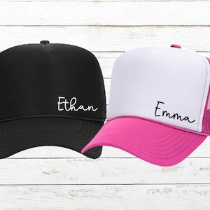 May include: Two trucker hats, one black with white text "Ethan" and one white with pink trim and black text "Emma".