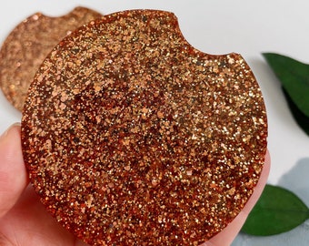 May include: A round, copper-colored coaster with a glitter finish. The coaster has a small, rounded cutout on the side.