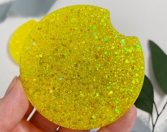 May include: A yellow glitter coaster with a cut-out for a drink. The coaster is made of resin and has a sparkly finish.
