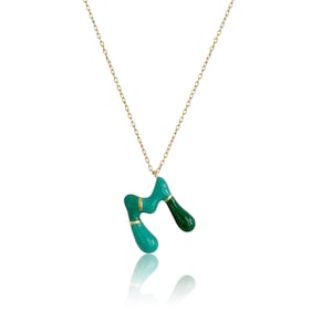 Puede incluir: Un collar de cadena dorada con un colgante abstracto verde y turquesa. El colgante está hecho de metal y tiene un acabado liso y brillante.