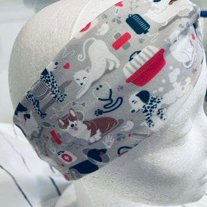 May include: A gray headband with a white background and a repeating pattern of dogs, cats, and pet-related items. The pattern includes a red and white bowl, a bone, a paw print, and a heart.