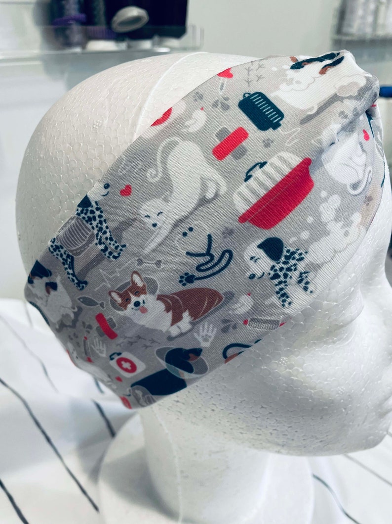 May include: A gray headband with a white background and a repeating pattern of dogs, cats, and pet-related items. The pattern includes a red and white bowl, a bone, a paw print, and a heart.