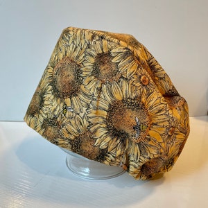 May include: A yellow and brown fabric scrub hat with a sunflower and bee print.