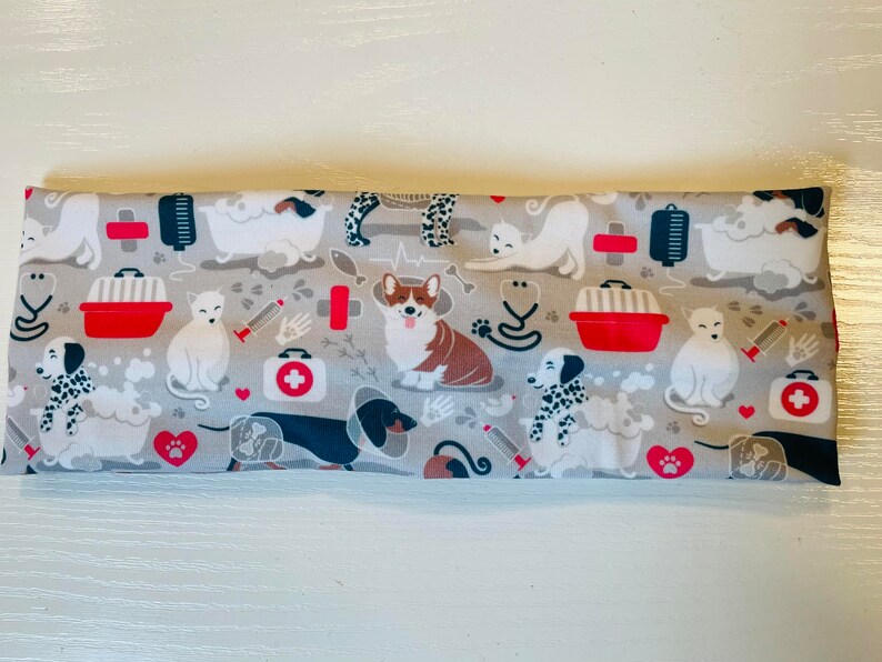 May include: A gray headband with a repeating pattern of dogs and cats in a veterinary theme. The pattern includes images of dogs and cats in a bathtub, a dog with a bandage, a cat in a carrier, and a first aid kit.