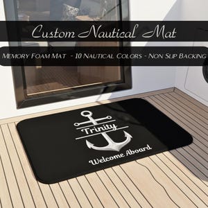 May include: Black rectangular memory foam mat with a white anchor design and the word "Trinity" above it. The mat also has the words "Welcome Aboard" below the anchor. The text "Custom Nautical Mat" is at the top.