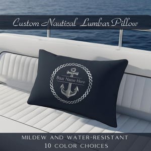 May include: A navy blue lumbar pillow with a silver anchor design inside a rope circle. The pillow has the text "Boat Name Here" and "Custom Nautical Lumbar Pillow". The pillow is mildew and water-resistant.