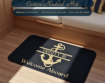 May include: A rectangular black memory foam mat featuring a gold anchor graphic, the text "TRINITY III" across the center, and the words "Welcome Aboard" printed in gold at the bottom. The mat has rounded corners and a non-slip backing.