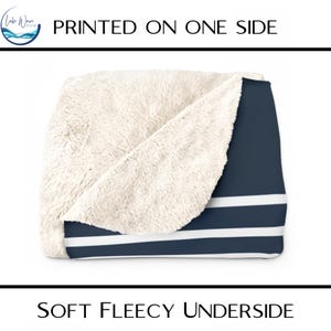 May include: A navy blue and white striped blanket with a soft, fleecy underside. The blanket has a white sherpa-like texture on the underside. The text "PRINTED ON ONE SIDE" and "SOFT FLEECY UNDERSIDE" are visible.