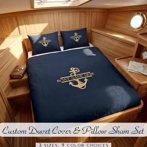 May include: Navy blue duvet cover and pillow sham set with a gold anchor design and the text "BOAT NAME HERE". The set includes two pillow shams and a duvet cover. The text "Custom Duvet Cover & Pillow Sham Set" is at the bottom.