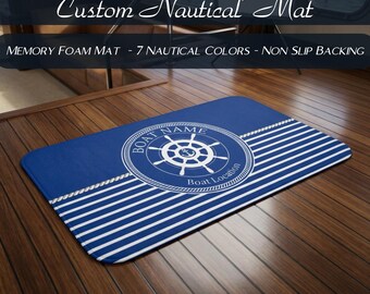 May include: A rectangular memory foam mat featuring a blue and white striped pattern with a central circular emblem containing a ship's wheel, an anchor, and the text "BOAT NAME" and "Boat Location" with a rope border design.