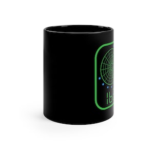May include: A black ceramic mug featuring a green radar screen graphic with a circular grid, a series of small blue dots, and digital green numbers at the bottom. The design is enclosed within a rounded green rectangular border on the side.