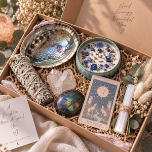May include: A gift box containing an iridescent abalone shell, a candle topped with blue crystals and dried flowers, a sage bundle, a clear quartz cluster, a dark labradorite stone, a Moon tarot card, and a selenite wand with dried foliage.