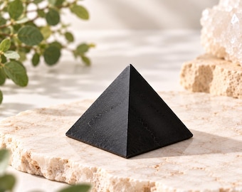 May include: A solid black pyramid with a smooth, matte finish and a square base. The object features clean, sharp edges and a pointed apex, displaying a uniform dark color throughout its four triangular faces and flat bottom surface.
