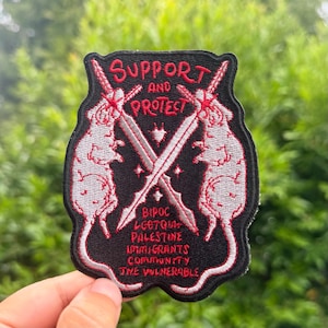 May include: A black embroidered patch featuring two white rats standing on their hind legs, each holding a crossed sword. The text reads SUPPORT AND PROTECT, followed by BIPOC, LGBTQIA+, PALESTINE, IMMIGRANTS, COMMUNITY, and THE VULNERABLE in red.