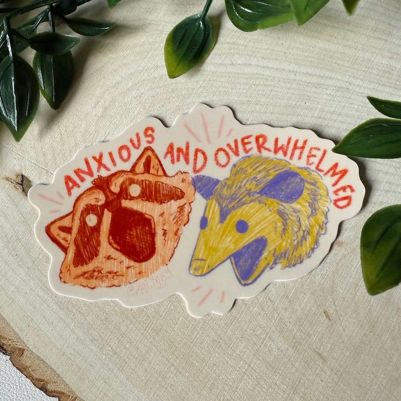 May include: A sticker with a raccoon and an opossum, with the text "anxious and overwhelmed" in red and orange lettering.