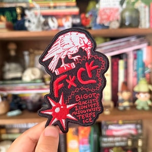 May include: A black embroidered patch featuring a white raven perched on a red book, with the red text F*CK and a red starburst. Below the star, red text lists: BIGOTS, RACISTS, ZIONISTS, MISOGYNISTS, TERFS, ICE. The patch has a black border.