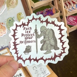 Op de afbeelding: Een sticker met een witte achtergrond en een donkerrode rand. De sticker toont een knielende ridder met een zwaard, een muis en de tekst "Fuck Ice Protect Your Neighbors."