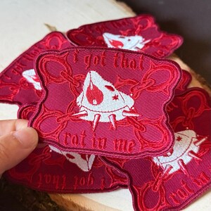 Può includere: Toppa ricamata bordeaux con la scritta "I got that rot in me". La toppa presenta una grafica bianca di una creatura stilizzata con una goccia rossa e dettagli a catena. Sono visibili diverse toppe.